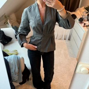 Grå blus/kavaj från Zara Woman - Säljer en stilren grå blus från Zara Woman med markerad midja och knäppning framtill. Använd fåtal gånger.
