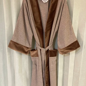 Skräddarsydd Kimono/Rock – Helt Ny - helt ny kimono/rock som är skräddarsydd av en skicklig sömmerska. Tyget är helt nytt och har aldrig använts. Plagget är i storlek one size och har en vacker brunmelerad färg med sammetsdetaljer i mörkbrun ton. Materialet är mjukt och behagligt med en lyxig känsla. Kimono/rocken har ett bälte i midjan för justerbar passform, två stora fickor framtill och är unisex, vilket gör att den passar både dam och herr.  Plagget är helt nytt och oanvänt, 