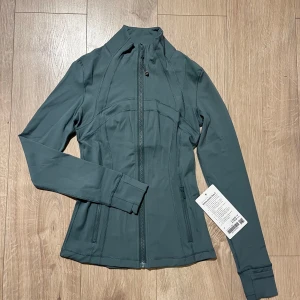 Ny grön lululemon jacka - Säljer en otroligt fin lululemon jacka i grön färg då den tyvärr är i fel storlek och kan ej lämna tillbaka då jag fick i present. Storlek 4 i nyskick! Färgen är svår att få tag på
