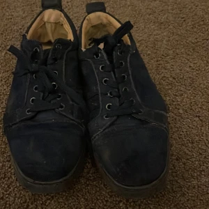 Svarta sneakers med röd sula - Svarta sneakers med snörning och rund tå. Skorna har en röd sula och beige insida. Ovandelen verkar vara i syntetmaterial och insidan är mjuk. Perfekta för dig som gillar en klassisk look med en färgklick under.