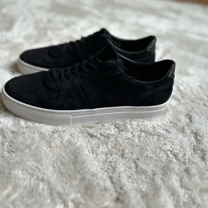 Svarta sneakers från Vagabond - Svarta sneakers från Vagabond med ovandel i mocka och klassisk vit platt sula. Skorna har snörning och en stilren, rund tå. Perfekta för dig som gillar en clean och enkel look med en touch av premiumkänsla. Köpta nya för 1400! Använd i en månad