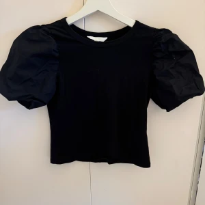 Svart topp med puffärmar från H&M - Svart topp från H&M med korta, voluminösa puffärmar och rund halsringning. Passar perfekt till jeans och kjol.