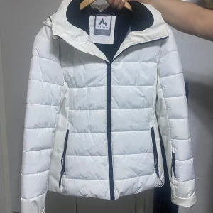 Ny Vit pufferjacka från McKinley (priset kan diskuteras vid snabb affär) - Snygg vit pufferjacka från McKinley med svarta detaljer och dragkedjor. Jackan har huva, två sidofickor med dragkedja och quiltad design. Perfekt för kalla dagar och har en sportig vibe. Fodrad insida för extra värme. Priset kan diskuteras vid snabb affär.