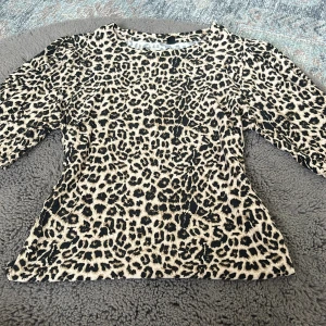 Leopardmönstrad topp i beige och svart XS - Säljer en snygg topp med leopardmönster i beige och svart. Modellen har trekvartsärm och rund halsringning. Tyget är mjukt och stretchigt, perfekt för dig som vill sticka ut med ett djurmönster. Passar dig som gillar trendiga och coola plagg. Lite stor storlek. Säljer den på grund av att den var för stor