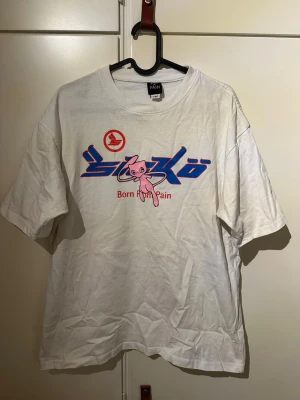 Vit Sicko T-shirt  - Vit t-shirt från Sicko med tryck i blått, rött och rosa framtill. Motiv med text och en tecknad figur på bröstet. Klassisk passform och rund halsringning. Perfekt för dig som gillar streetwear och unika prints. Lite smuts fläck vit armhålor.