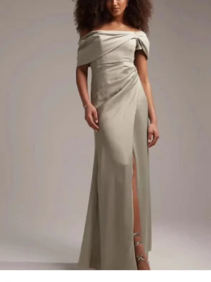 Grön offshoulder maxiklänning - Stilren grön maxiklänning med offshoulder-design och draperad överdel. Klänningen har en elegant slits framtill och smickrande passform. Perfekt för dig som vill ha en sofistikerad look med modern twist.
