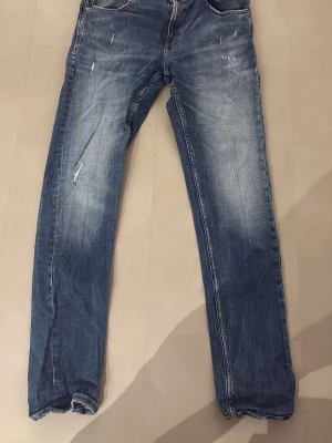 Replay jeans med slitningar - Replay jeans  med raka ben och snygga slitningar framtill. Jeansen har fem fickor, knappgylf och en mörkblå tvätt med ljusare partier. Perfekta för en avslappnad och trendig look.