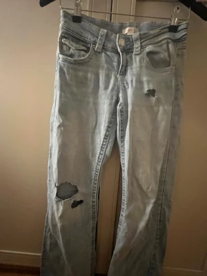 Ljusblå ripped jeans med raka ben - Snygga ljusblå jeans med slitna detaljer och hål på låret och vid fickan. Jeansen har klassisk femficksdesign, raka ben och normal passform. Perfekta för en avslappnad och trendig look.