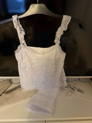 Vit spetslinnetopp - Supersöt vit linnetopp med breda axelband och volangdetaljer. Toppen är täckt av spets och har en croppad passform som ger en trendig look. Perfekt att styla med jeans eller kjol för en fräsch outfit. Linnet har dubbel tyg så man ser inte bhn igenom. Köpt på SHEIN ordpris: 100kr säljer för 50kr och använt 1 gång 