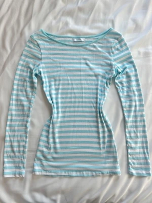 Ljusblå och vit randig långärmad topp - Säljer en långärmad topp från Aéropostale med ljusblå och vita horisontella ränder. Toppen har en figurnära passform och rundad halsringning. Perfekt för dig som gillar en enkel men fräsch stil. Den e dock lite genomskinlig 