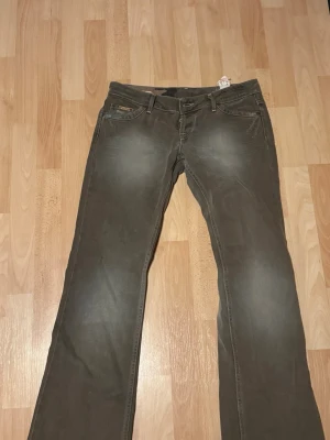 Brun/grön bootcut jeans från Glago  - Snygga brun/gröna jeans från Glago med bootcut-passform och klassiska fem fickor. Jeansen har en lätt tvättad look och dekorativa sömmar. Den är liten i storlek och aldrig använd men har tyvärr ingen prislapp kvar. 