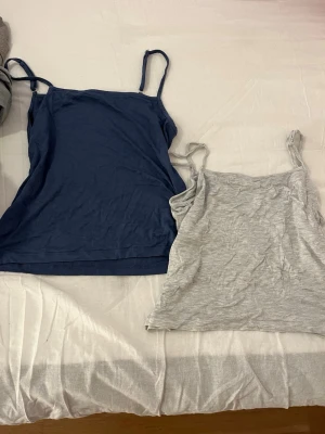 Två linne-toppar i blått och grått - Säljer två enkla och bekväma linne-toppar med smala axelband, en i marinblått och en i ljusgrått. Perfekta att matcha med jeans eller shorts. Båda är i mjuk bomull och har en klassisk, rak passform.
