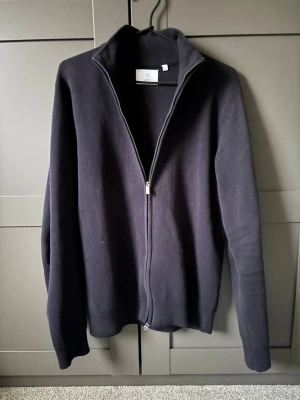 Mörkblå ziptröja från Bläck - Stilren svart ziptröja från Bläck med hög krage och hel dragkedja framtill. Tröjan är tillverkad i mjukt material och har ribbade muddar vid ärmslut och nederkant. Perfekt för lager-på-lager och enkel att matcha med andra plagg. Tröjan är endast använd en gång! Nypris:749!