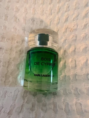 Bois de Cypres parfym Karl Lagerfeld - En snygg parfymflaska i glas med grön toning och silverfärgat lock. Doften heter Bois de Cypres från Karl Lagerfeld och flaskan har en modern, rund form. Perfekt för dig som gillar fräscha och träiga dofter.