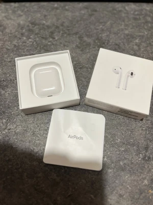 Apple AirPods 2 - Säljer ett par vita Apple AirPods 2 med laddningsetui. Snygg och stilren design i blank plast, perfekt för dig som vill ha smidiga och trådlösa hörlurar till mobilen. Kommer i originalförpackning med tillhörande manual. Skal ingår vid begäran.