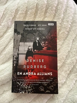 En andra allians av Denise Rudberg - Spännande roman av Denise Rudberg, andra delen i serien Kontrahenterna. Boken har ett svart, vitt och rött omslag med motiv av tre kvinnor och skrivmaskinstangenter. Handlingen utspelar sig i Stockholm under andra världskriget och kretsar kring kvinnliga kodknäckare.
