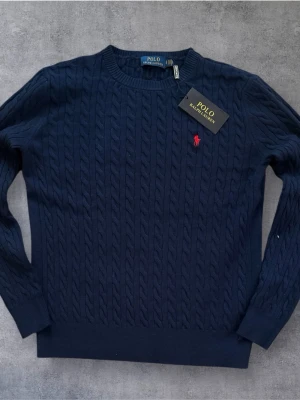 Polo Ralph Lauren Kabelstickad Tröja – Marinblå – Strl S – Ny med Tag - • Märke: Polo Ralph Lauren • Modell: Klassisk kabelstickad tröja (Cable Knit) • Färg: Marinblå / Navy • Storlek: S • Skick: Helt ny med originaltag kvar • Material: Mjuk och högkvalitativ bomullsblandning  Priset kan diskuteras!!