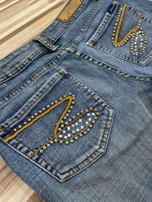Blå bootcut jeans med pärldetaljer - Säljer ett par blå jeans från Seven7 med bootcut passform. Jeansen har snygga pärldetaljer och gul brodyr på bakfickorna samt pärlor längs fickkanterna fram. Med låg midja och coola detaljer. As coola storlek 26 vilket motsvarar 34 i jeans. Midjemått: 35cm tvärsöver. Innerbenslängd: 81cm. Pris går att diskutera, kom privat vid önskan av fler bilder💝💝
