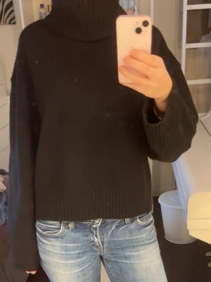 Svart polotröja i stickat material - Mysig svart polotröja i stickat material med bred ribbad kant nedtill och vid ärmslut, jättesnygg. Passar S-M