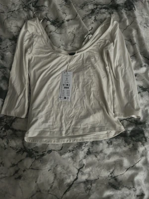 Vit omlottopp med djup rygg - Trendig vit omlottopp med djup, öppen rygg och trekvartsärm. Tillverkad i mjuk bomullsmix som känns skön mot huden. Perfekt för dig som vill ha en enkel men snygg topp med unik skärning.