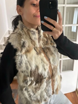 Beige och brun pälsväst med dragkedja - Snygg pälsväst i beige, bruna och grå toner med fluffig känsla och dragkedja framtill. Västen har en kortare modell och är perfekt för att ge din outfit en trendig touch. Passar till både jeans och kjol för en cool look.