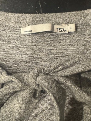 Grå cardigan med knyt från Lager 157 - Mysig gråmelerad cardigan från Lager 157 med knytband framtill. Tröjan har långa ärmar och en mjuk, stretchig känsla. Perfekt att slänga över en topp för en avslappnad look. Enkel och stilren design som passar till det mesta.