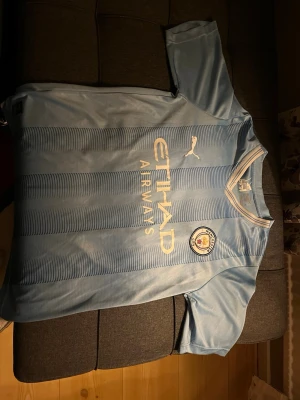 Manchester City matchtröja Puma - Ljusblå Manchester City matchtröja från Puma med Etihad Airways-tryck på bröstet och klubbmärke. Nummer 25 och namnet Akanji på ryggen. Tillverkad i lätt och ventilerande material, perfekt för fotbollsträning eller match.