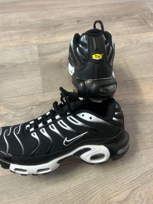 Nike TN Air Max Plus svarta sneakers - Svarta Nike Air Max Plus sneakers med vita och silverfärgade detaljer. Klassisk Tn-logga på hälen, vågformade linjer på ovandelen och vit sula med synlig dämpning. Skorna har snörning och är tillverkade i syntetmaterial och mesh för en sportig look. Helt nya 