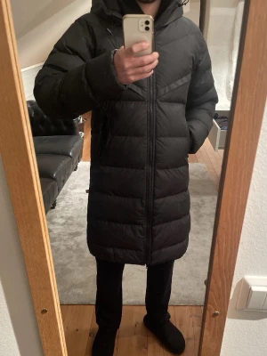 Svart lång pufferjacka från Nike XS - Säljer en svart lång pufferjacka från Nike med huva och Storm-FIT-teknologi. Jackan har två dragkedjeförsedda fickor, hel dragkedja framtill och diskret Nike-logga på bröstet. Perfekt för kalla dagar när du vill hålla dig varm och stilsäker.