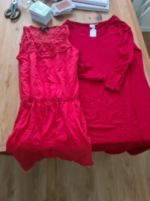 Två röda klänningar - Säljer två röda klänningar. Ena är ärmlös med spetsdetaljer upptill och rund hals, den andra har lång ärm och enkel design. Perfekta för dig som gillar färgstarka plagg och vill ha olika stilar att välja mellan.