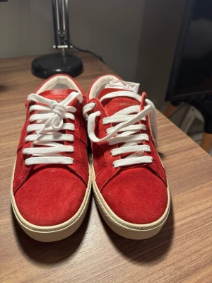 Saint Laurent skor - Saljer ett par Saint Laurent-sneakers i en ovanlig röd mocka-finish. Skicket är utmärkt. Jag köpte dem för ungefär tva år sedan, men de kändes lite för smala för mina fötter och har darför mest stått oanvända i garderoben. Nyligen lämnade jag in dem till en professionell skovård för rengöring, borttagning av damm och en ny impregneringsbehandling. Skorna är redo att anvandas och ser nastan nya ut. Box och dust bags ingår.