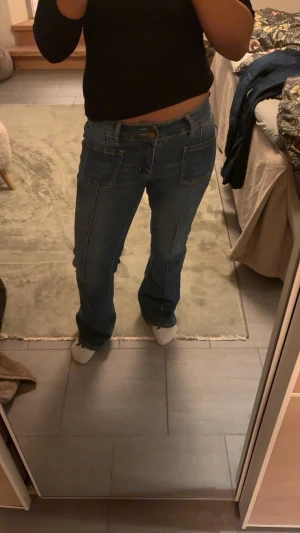 Blå bootcut jeans med fickor - Säljer ett par blå bootcut jeans med stora fickor fram och bak. Jeansen har kontrastsömmar och en klassisk midja. Perfekta för en avslappnad och trendig look.