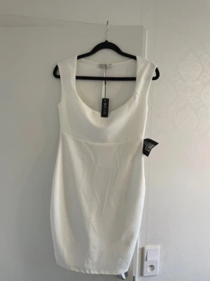 Vit  klänning från NLY One - Stilren vit klänning från NLY One med djup rundringning och figurnära passform. Klänningen är ärmlös och har en enkel, elegant design som passar perfekt till många olika tillfällen.  Klänningen är ny och aldrig använd, med lappen fortfarande kvar. 