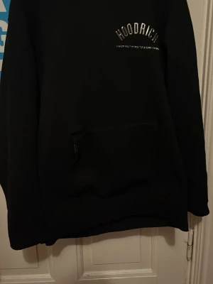 Hoodrich hoodie - Säljer en svart hoodie från Hoodrich med stor logga och texten 'FROM NOTHING TO SOMETHING' både fram och bak. Hoodien har en klassisk känguruficka och huva. Perfekt för dig som gillar streetwear och vill ha en stilren men ändå fet look.