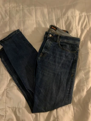 Blå jeans från BOSS, storlek 31/32 - Säljer ett par klassiska blå jeans från BOSS i storlek 31/32. Jeansen har , snygga denim jeans med rak passform och normal midja.