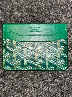 Grön  plånbok  - Snygg grön plånbok  med klassiskt mönster och flera kortfack. Tillverkad i skinn med ikoniska tryck i vitt och beige. Perfekt för kort och sedlar, smidig att ha i fickan. Fraktar samma dag😁👍
