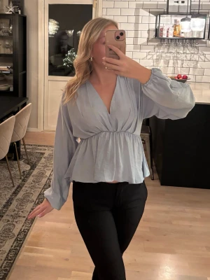 Ljusblå v-ringad blus  - NA-KD - Superfin ljusblå blus med v-ringning och volang nedtill. Blusen är i storlek 32 men passar perfekt till mig som vanligtvis har storlek 34. Stretchig i midjan. Publicerad på flera säljsidor. 