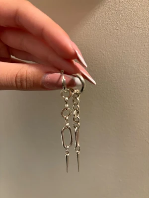 Örhängen L8Hasselblad - Säljer ett par unika silvriga statementörhängen från L8Hasselblad. Örhängena har kedjedetaljer och spetsiga hängen som ger en edgy vibe. Perfekta för dig som vill sticka ut och addera något extra till din look. Kommer i originalask. 