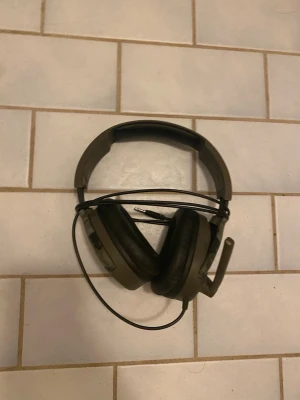 Svart gamingheadset med mikrofon - Säljer ett svart over-ear gamingheadset med kabel och inbyggd mikrofon. Hörlurarna har mjuka öronkuddar och justerbart huvudband för skön passform. Perfekt för gaming eller videosamtal, ansluts via 3,5mm-kontakt.