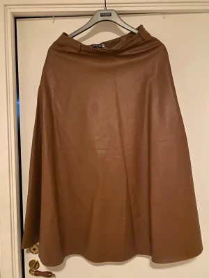 Brun långkjol i skinnimitation från Pita - Säljer en snygg brun långkjol från Pita Istanbul i skinnimitation. Kjolen har en enkel och stilren design med lätt utställd form. Perfekt för dig som vill ha en trendig och tidlös look.