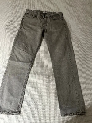 Grå Jack Jones 501 raka jeans - Snygga grå Levi's 501 jeans med klassisk rak passform och fem fickor. Jeansen har en tidlös look med knappgylf och är tillverkade i slitstarkt bomullsjeansmaterial. Perfekta för dig som gillar en clean och enkel stil.