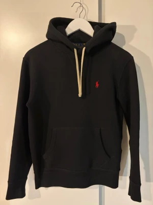 Svart Polo Ralph Lauren hoodie - Svart hoodie från polo ralph lauren i storlek xs. Är själv 174cm. Köpt ifrån Zalando och har använts ett fåtal gånger. Säljs för att jag inte längre använder plagget. 