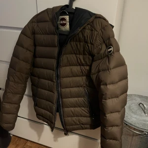 Brun pufferjacka från Colmar, strl 46 - Säljer en brun pufferjacka från Colmar med klassisk logga på ärmen. Jackan har dragkedja framtill, två fickor med dragkedja och en snygg quiltad look. Perfekt för kyliga dagar och riktigt skön att bära.