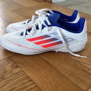 Adidas vita och blå inomhus skor  - Säljer ett par Adidas fotbollsskor i vitt med blå och röda detaljer. Endast använda ett par gånger. 