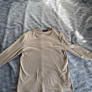 Beige långärmad tröja Polo Ralph Lauren - Snygg beige långärmad tröja från Polo Ralph Lauren i bomull. Tröjan har rund halsringning och den klassiska broderade loggan på bröstet. Perfekt för dig som gillar stilrena och tidlösa plagg med en clean look. Skick 9/10