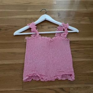 Rosa smockad linnetopp med volang - Supersöt rosa linnetopp med smockat tyg och volangdetaljer vid axelband och nederkant. 