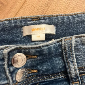 Blå low waist  bootcut jeans från Gina Tricot - Snygga blå jeans från Gina Tricot i storlek 152. Modellen har bootcut-ben, klassiska fem fickor och dubbla knappar fram. Jeansen har en lätt tvättad look och är tillverkade i jeansmaterial med sköna sömmar och detaljerade bakfickor.