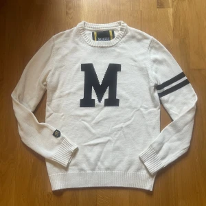 Stickad tröja från Morris - Cremefrägad  stickad tröja från Morris med stor svart M på bröstet och två marinblåa ränder på ena ärmenⓂ️| skriv vid funderingar, priset är ej hugget i sten !