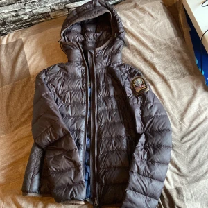 Parajumpers dunjacka XS mörkblå - Snygg mörkblå dunjacka från Parajumpers i superlätt material. Jackan har huva, dragkedja framtill och klassisk PJS-patch på ärmen. Perfekt för kalla dagar och riktigt skön att bära. Passformen är normal och jackan är quiltad för extra värme.