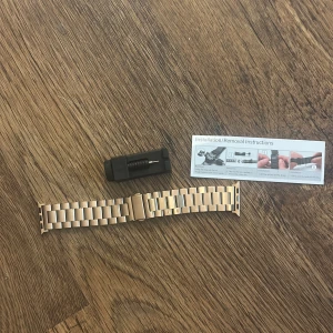 Guldfärgat metallarmband till applewatch - Snyggt guldfärgat metallarmband till klocka med klassisk länkdesign. Armbandet har en viklås och kommer med verktyg för enkel justering samt instruktioner. Perfekt för dig som vill ge din klocka en lyxig och modern look. 38/40/41 aldrig använd